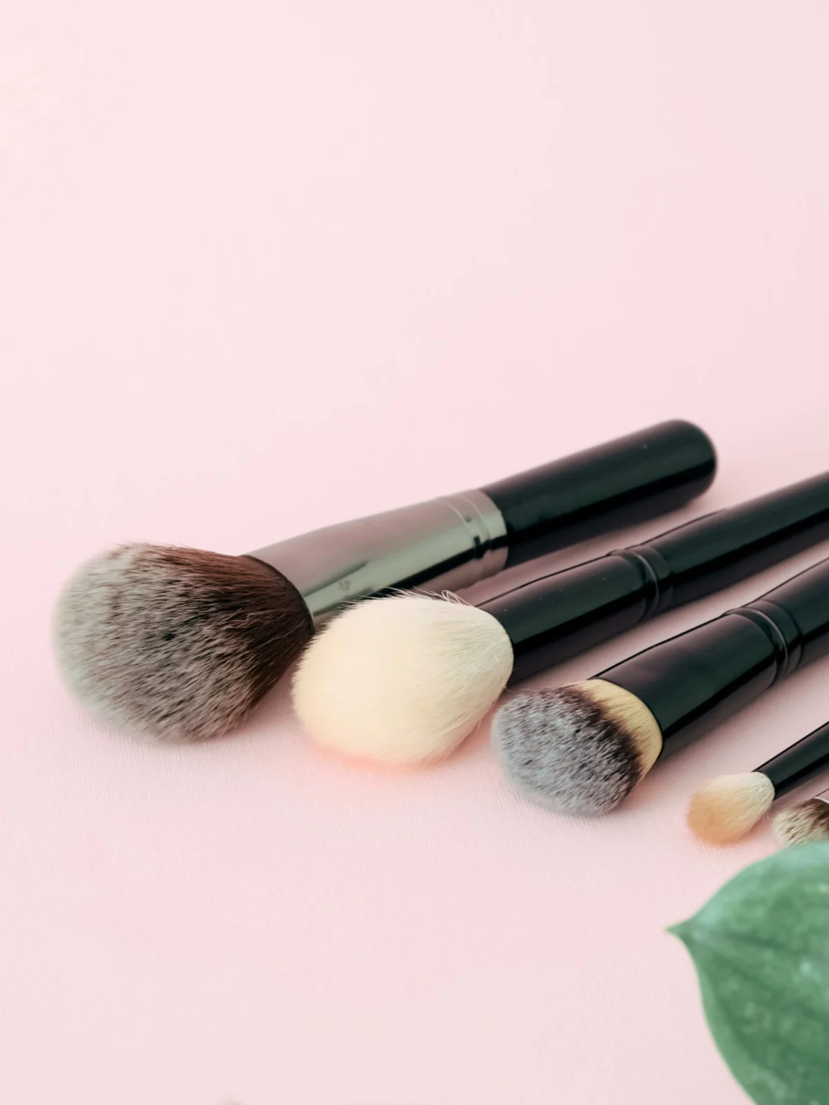 Real makeup brushes arranged on a pastel pink surface
