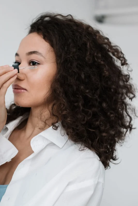 A woman with curly hair applying a skincare product to her face